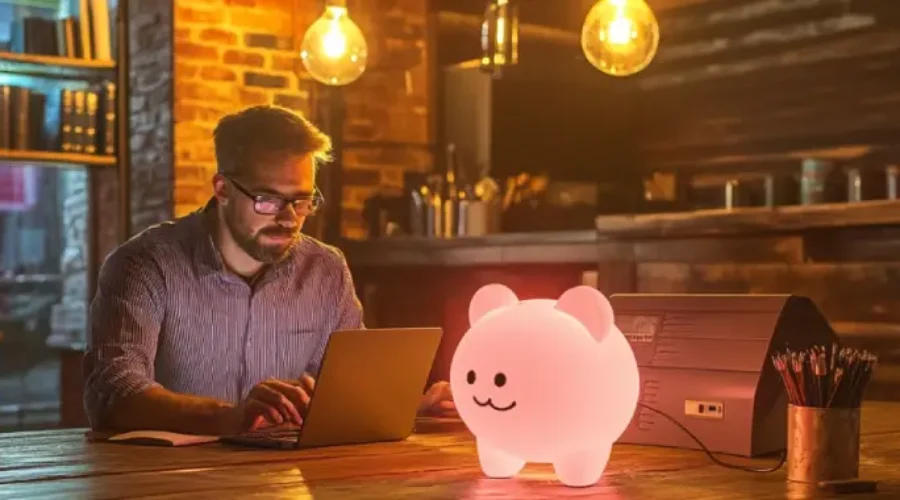 A man working on a laptop in a warmly lit café with a glowing piggy bank-managed it services for small businesses